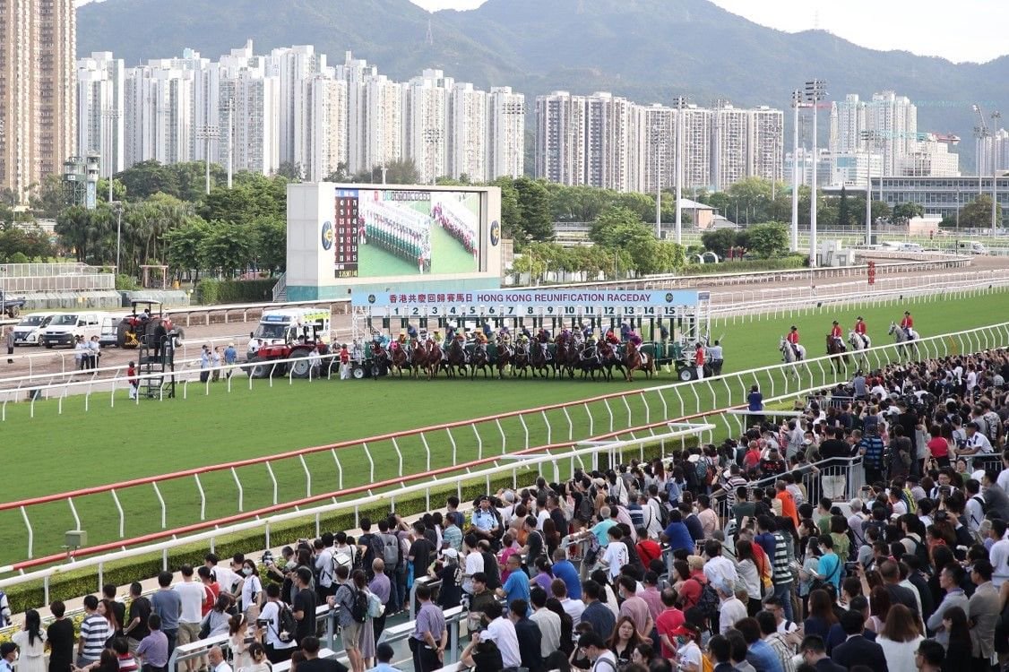 香港沙田馬場賽事現場，賽馬起步閘打開的瞬間，眾馬齊奔，觀眾席人頭湧湧，展現出香港賽馬日的緊張氣氛與高人氣。